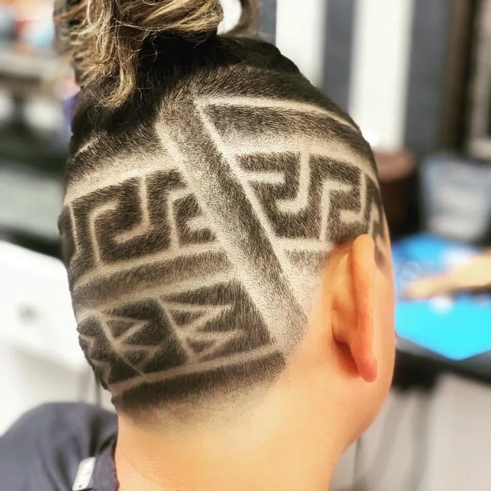 Geometric pattern shaved into the side and back of a client's head, with sharp interlocking lines and a top knot